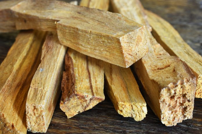 A close up image of palo santo smudge sticks on a dark wood table.