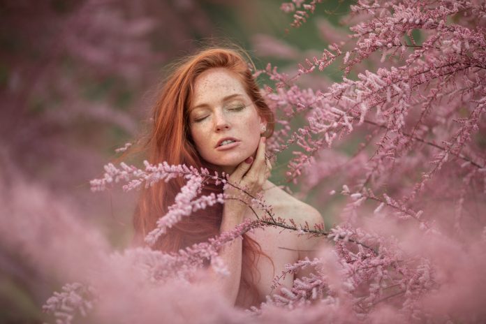 Portret z bliska kobiety w różowych gałęziach kwitnącego drzewa brzoskwiniowego.
