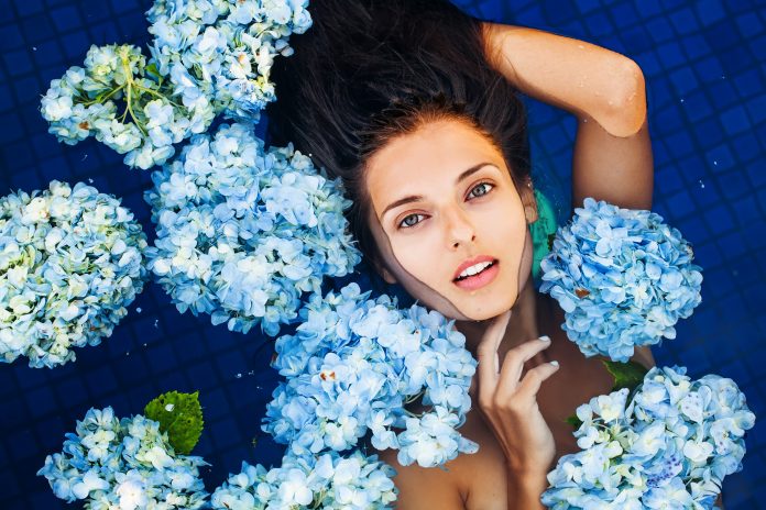 dramatic portrait of a woman floating an a swimming pool full of flowers (macro, blue filter)