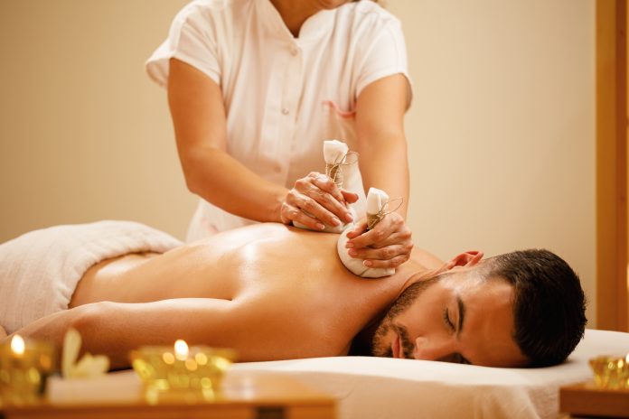 Relaxed man enjoying in back massage with herbal compress during spa treatment.