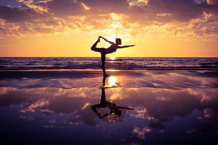sylwetka kobiety ćwiczącej jogę na plaży przy zachodzie słońca