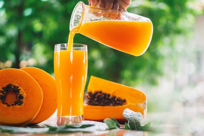 woman hand pouring papaya juice on glasses with slice papaya on wooden background, healthy and diet fruit