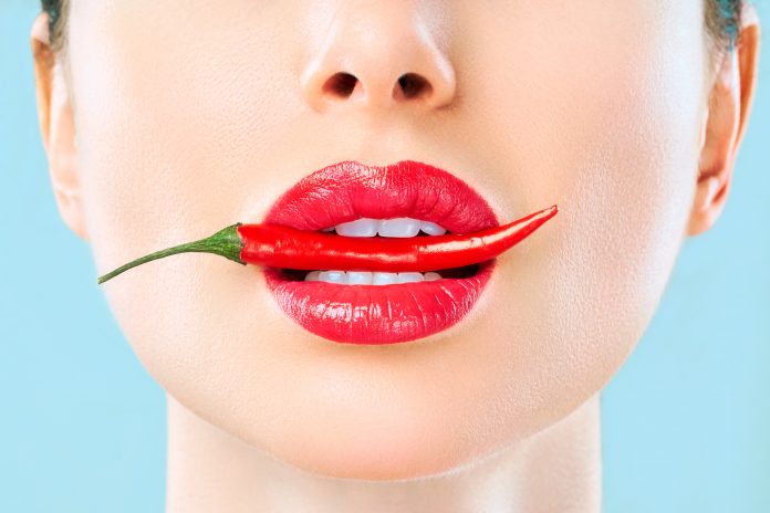 Young woman with chili red pepper isolated en blue background. Sexy female lips. Hot seductive girl.