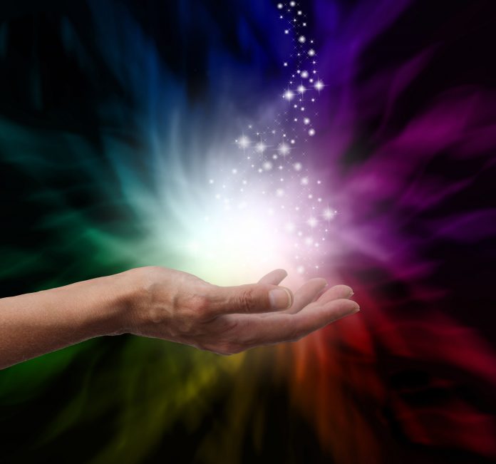 Healer's hand outstretched into magical healing energy field with sparkles floating up and away