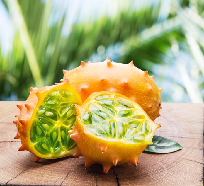 Kiwano fruits on the wooden table with green nature on the background.