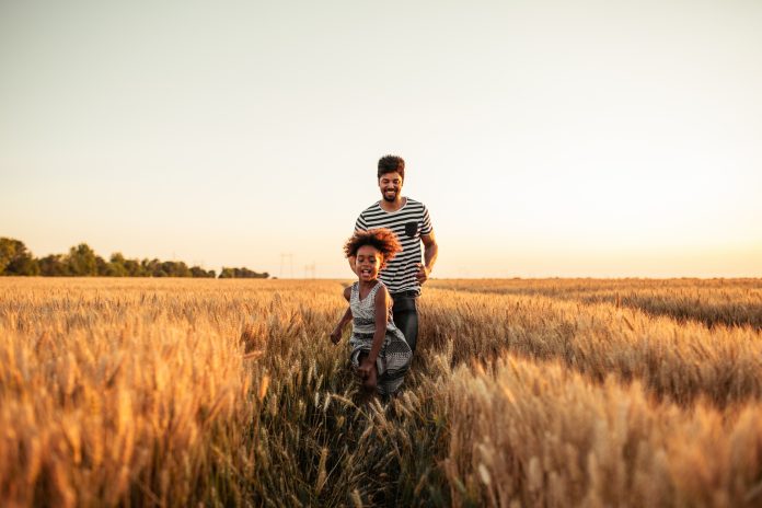 Photo of an african american father and daughter running trough the fields together.