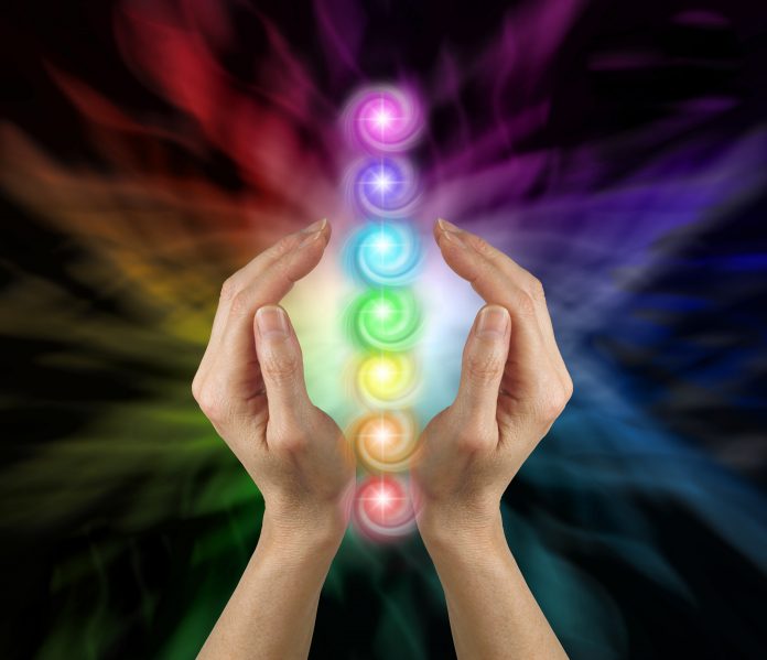 Female parallel hands against a multicoloured background of energy and the Seven Chakras floating between her hands