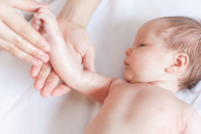 Mamma gör massage för lycklig baby, applicerar olja på handen, med vit bakgrund