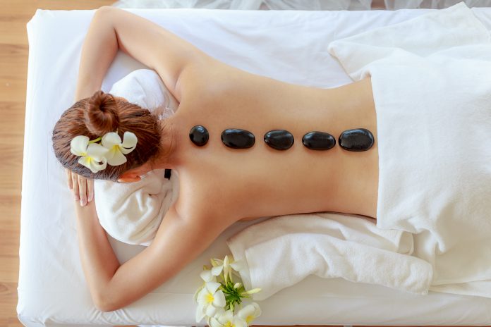 Top view of  young beautiful woman receiving hot black marble stone massage and relaxing in spa salon