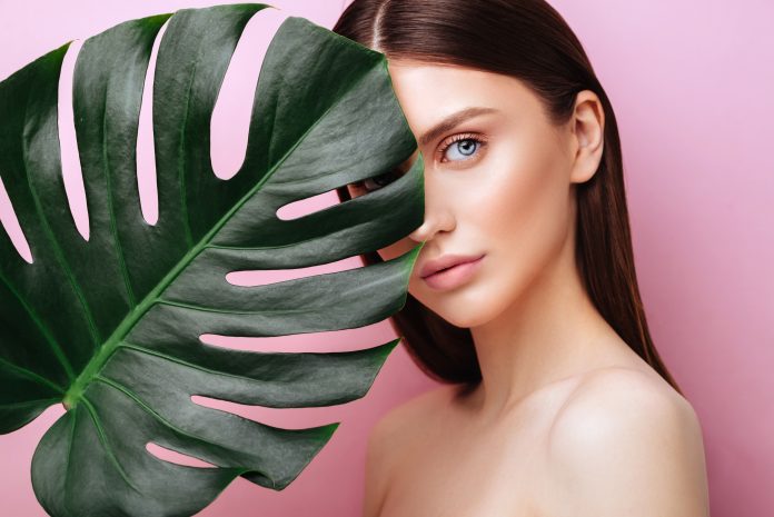 Beauty Woman with natural green palm leaf Portrait, model girl with perfect makeup, natural eyeshadows. Brunette Beautiful Fashion Model Girl Face. Skin care. Perfect Skin. On pink Background