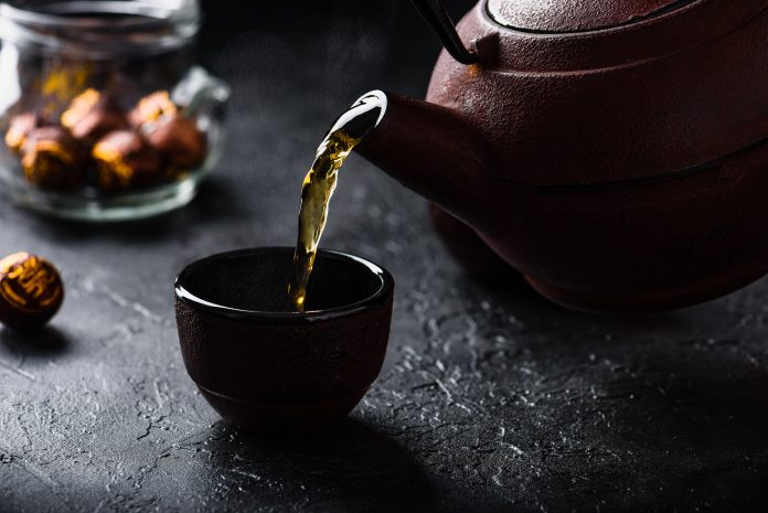 Versare il tè rosso pronto dal bollitore di ferro nella teiera