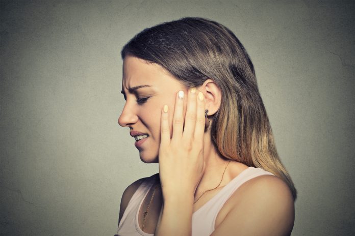 Acufene. Primo piano del profilo laterale di giovane donna malata con dolore all'orecchio che si tocca la testa dolorante isolato su sfondo blu