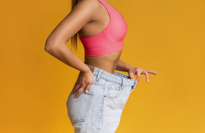 Weight Loss Concept. Profile Portrait Of Fit Girl Posing In Oversize Jeans Over Yellow Background, Cropped Image With Copy Space