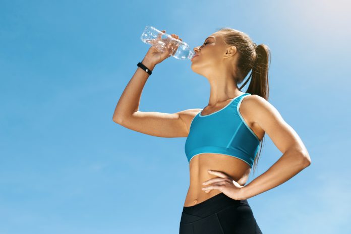Woman Drinking Water After Running. Portrait Of Beautiful Athletic Girl In Bright Colorful Sportswear Resting After Fitness Workout, Drink Water From Bottle On Blue Sky Background. High Quality Image