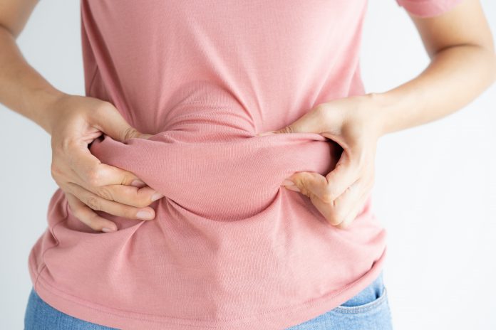 Mujer mano sosteniendo su propia grasa del vientre y la celulitis en el fondo blanco. Las mujeres antes de la pérdida de peso y la forma del concepto de músculo del estómago saludable.