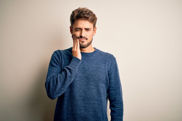 Young handsome man with beard wearing casual sweater standing over white background touching mouth with hand with painful expression because of toothache or dental illness on teeth. Dentist