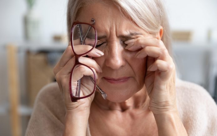 Close up of unhealthy elderly woman take off glasses massage eyes suffering from strong migraine or headache, unwell sick senior female grandmother struggle with blurry vision or dizziness at home