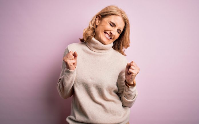 Mittleres Alter schöne blonde Frau trägt lässig Rollkragenpullover über rosa Hintergrund aufgeregt für den Erfolg mit erhobenen Armen und Augen geschlossen feiernden Sieg lächelnd. Gewinner-Konzept.