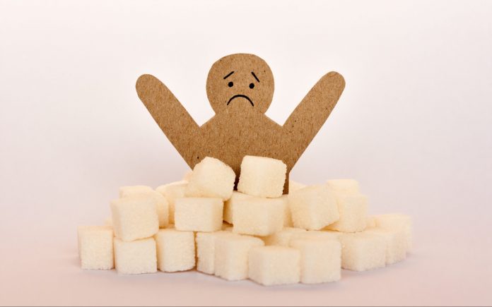Сахарная зависимость, инсулинорезистентность, нездоровое питание, фигура картонного человека в окружении кубиков рафинированного сахара на белом фоне, медицинская концепция защиты от диабета