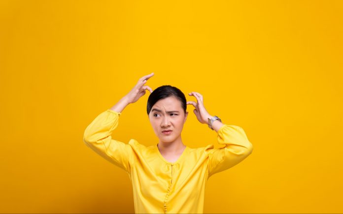 Woman scratching her head isolated over yellow background