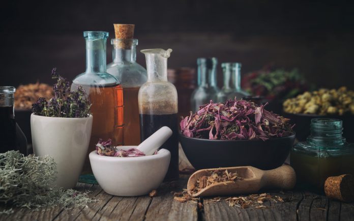 Bottles of healthy tincture or infusion, mortar and bowls of medicinal herbs on wooden table. Herbal medicine.