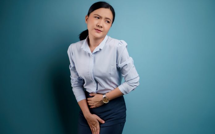 Asian woman having painful holding hands pressing her crotch lower abdomen isolated on background.