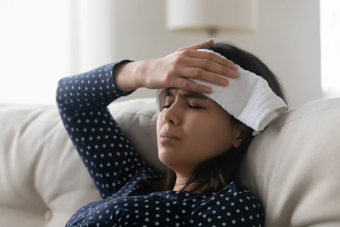 Close up unhealthy upset sick Asian young woman holding wet towel on forehead, suffering from fever, cold, flu or grippe, health problem concept, unhappy frustrated female feeling unwell