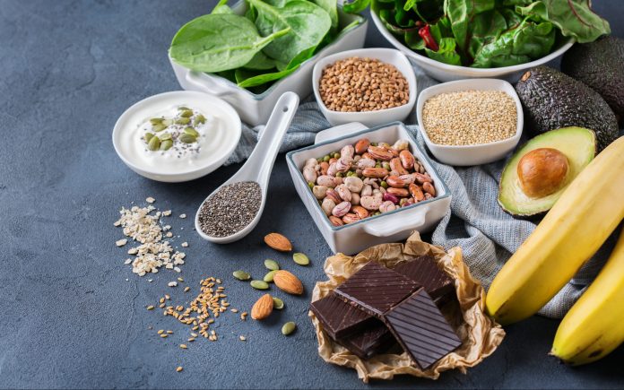 Healthy food nutrition dieting concept. Assortment of high magnesium sources. Banana chocolate spinach chard, avocado, buckwheat, sesame chia flax seeds, yogurt, nuts, beans oat. Copy space background