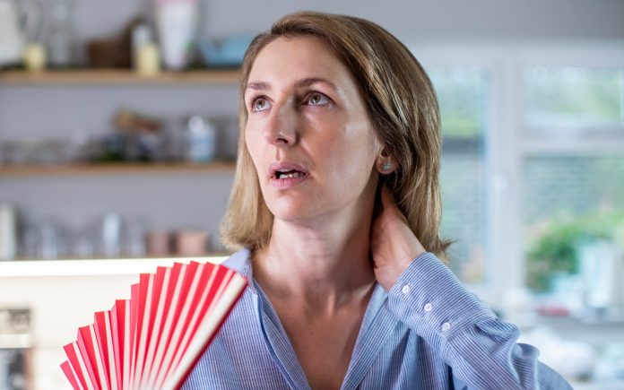 Mature Woman Experiencing Hot Flush From Menopause Using Fan