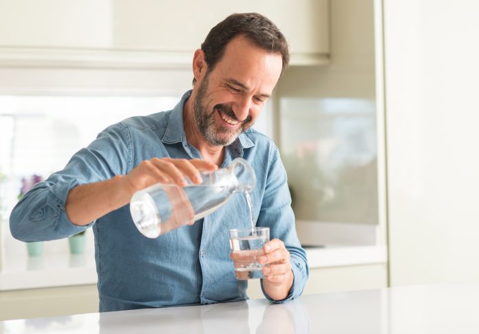 Mittleres Alter Mann trinkt ein Glas Wasser mit einem glücklichen Gesicht stehen und lächelnd mit einem zuversichtlichen Lächeln zeigt Zähne