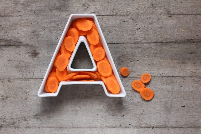 Vitamin A in food concept. Plate in the shape of the letter A with sliced fresh carrots on wooden background. Flat lay or top view.
