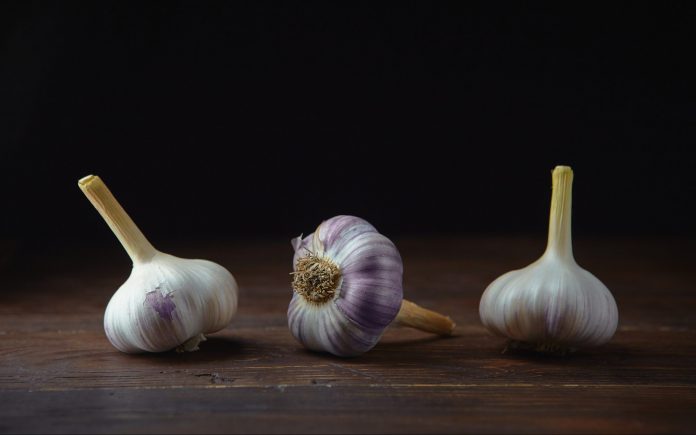 Horizontal view of three garlic heads on a black wooden background.