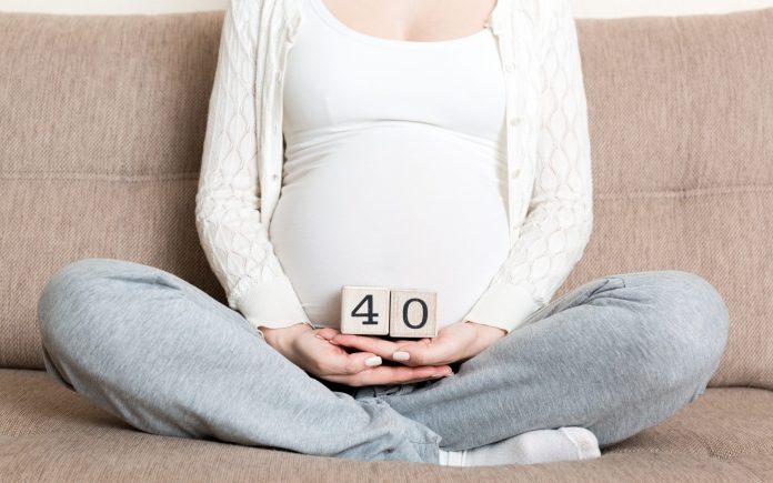 Donna incinta in biancheria intima bianca sul letto di casa con in mano il calendario con le settimane 40 di gravidanza. Concetto di maternità. Aspettativa di un bambino in arrivo.