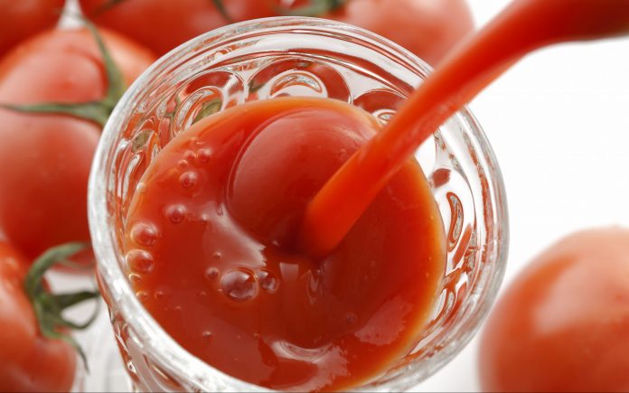 Tomatensaft wird in ein Glas auf weißem Hintergrund gegossen