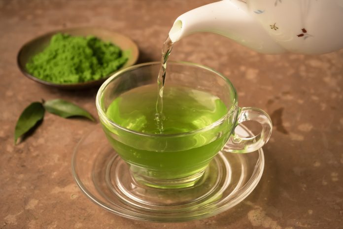 Grüner Tee wird auf dem Tisch in eine gläserne Teetasse gegossen