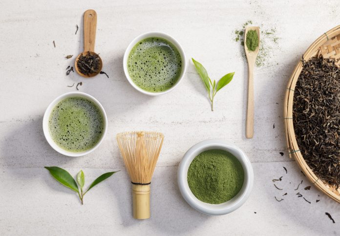 Polvere di tè verde matcha biologico in una ciotola con frusta a filo e foglia di tè verde su un tavolo di pietra bianca, prodotto organico dalla natura per la salute con stile tradizionale