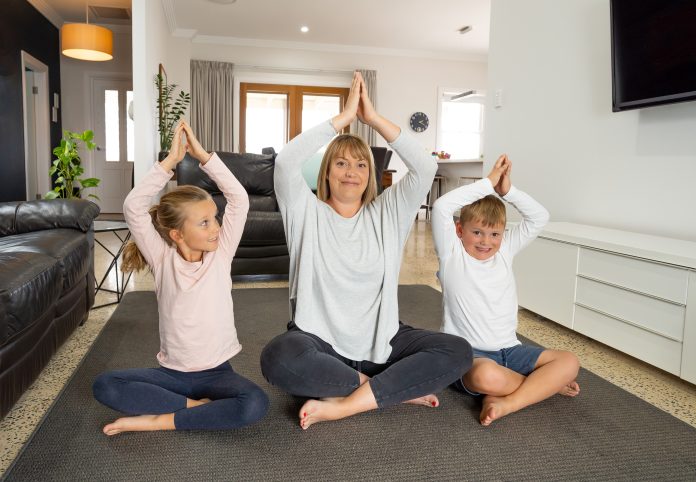 Famiglia caucasica che fa yoga a casa in quarantena. Madre, figlia e figlio fanno meditazione durante la quarantena. Salute, esercizio fisico a casa e cura di sé per l'isolamento da coronavirus.